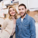 A young couple standing in front of a water heater in a store. Heaterwise